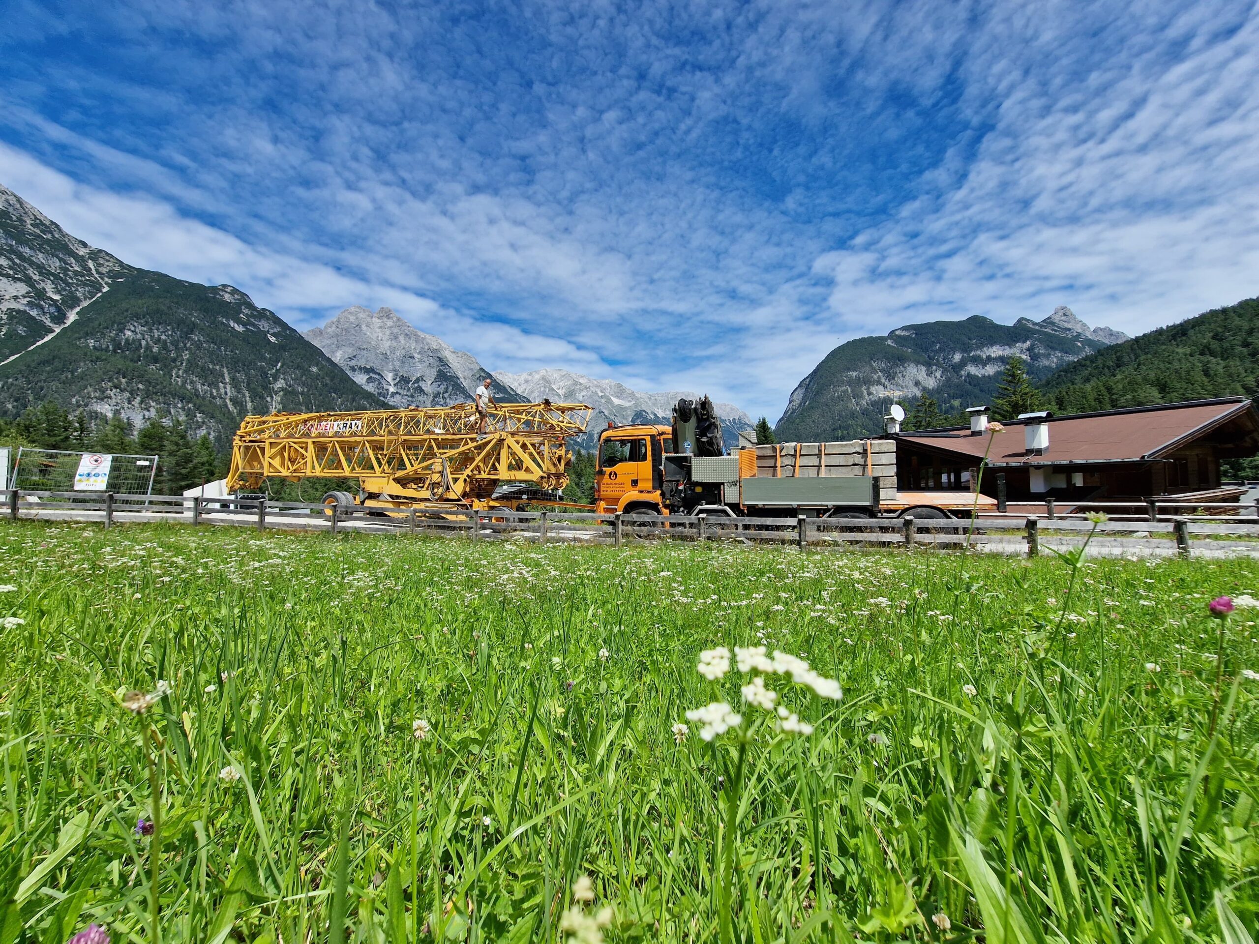 Lastwagen von Da Darchinger transportiert einen großen Baukran durch eine alpine Landschaft.