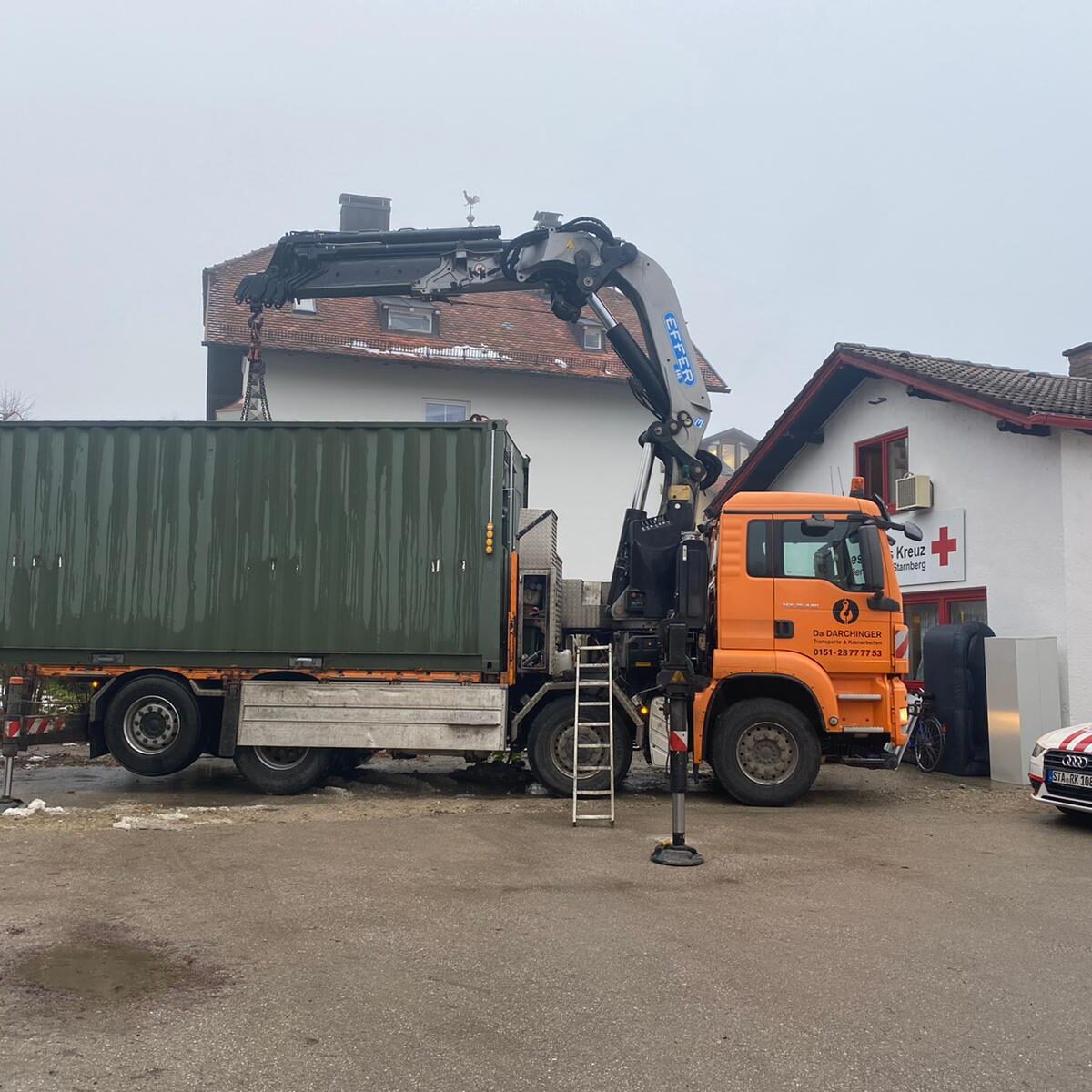 Kranfahrzeug von Da Darchinger beim Verladen eines grünen Containers auf einem Firmengelände.